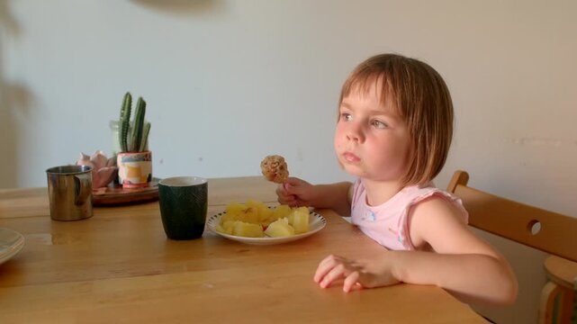 white toddler thoughtful at breakfast table holding fork and looking away, pensive expression, plate of pancakes and cup