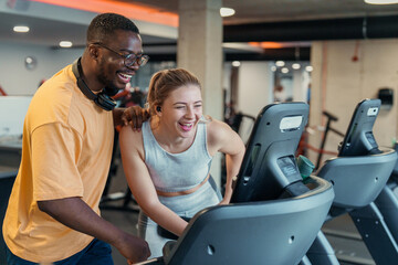Joyful diverse man and woman exercising together on treadmill in modern gym with fitness equipment