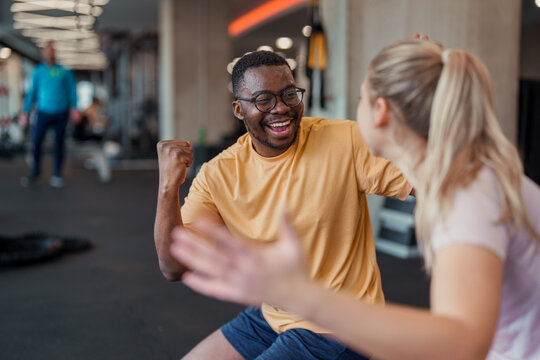 Joyful Middle-Aged Black Man In Yellow Shirt Laughing With Blonde Female Partner During Fitness Training Session