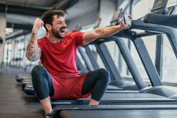 Bright indoor gym lighting energetic bearded man in red shirt taking selfie celebrating