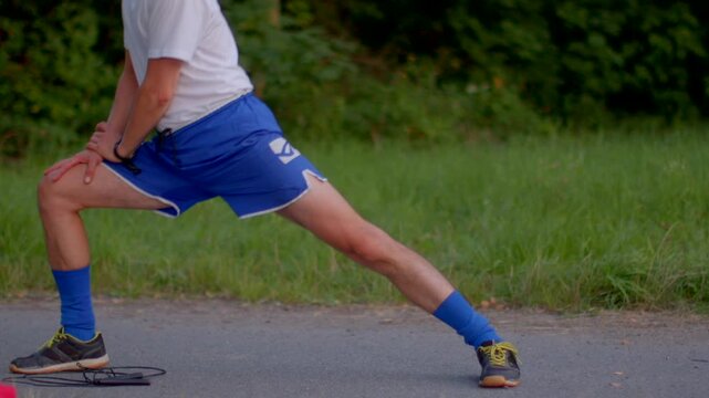 white male lunge stretch on roadside focusing on hamstring calf mobility hands on knee steady breathing blue shorts