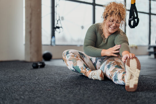 Athletic Young Woman With Blonde Curls Relaxing On Exercise Mat In Modern Fitness Center After Training
