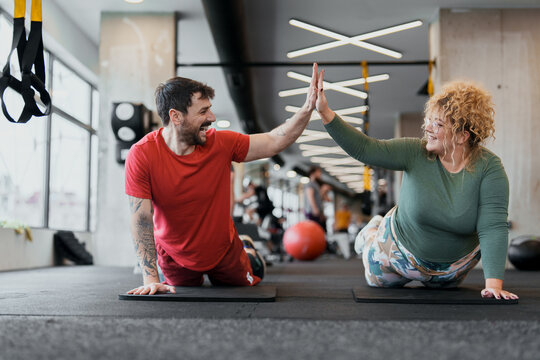 Smiling Caucasian Man and Woman Exercising Together High Fiving in Bright Gym Setting