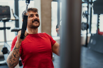 Young athletic man exercising with cable machine in modern gym smiling and focused