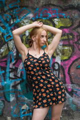 Blonde sensual woman with long legs posing confidently in front of a colorful graffiti wall, wearing a short floral dress. Urban fashion meets vibrant street art in this expressive portrait.