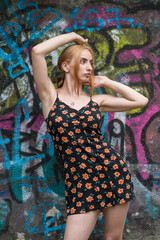 Blonde sensual woman with long legs posing confidently in front of a colorful graffiti wall, wearing a short floral dress. Urban fashion meets vibrant street art in this expressive portrait.