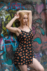 Blonde sensual woman with long legs posing confidently in front of a colorful graffiti wall, wearing a short floral dress. Urban fashion meets vibrant street art in this expressive portrait.