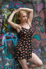 Blonde sensual woman with long legs posing confidently in front of a colorful graffiti wall, wearing a short floral dress. Urban fashion meets vibrant street art in this expressive portrait.