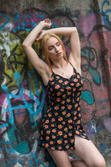 Blonde sensual woman with long legs posing confidently in front of a colorful graffiti wall, wearing a short floral dress. Urban fashion meets vibrant street art in this expressive portrait.