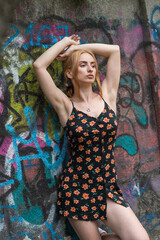 Blonde sensual woman with long legs posing confidently in front of a colorful graffiti wall, wearing a short floral dress. Urban fashion meets vibrant street art in this expressive portrait.