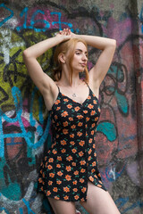 Blonde sensual woman with long legs posing confidently in front of a colorful graffiti wall, wearing a short floral dress. Urban fashion meets vibrant street art in this expressive portrait.