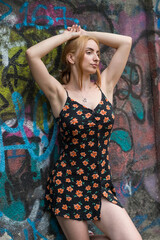Blonde sensual woman with long legs posing confidently in front of a colorful graffiti wall, wearing a short floral dress. Urban fashion meets vibrant street art in this expressive portrait.