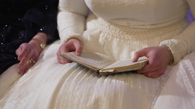 A close-up of a bride in a white lace dress holding a prayer book. This intimate and serene moment captures tradition and faith, ideal for wedding or religious-themed content.