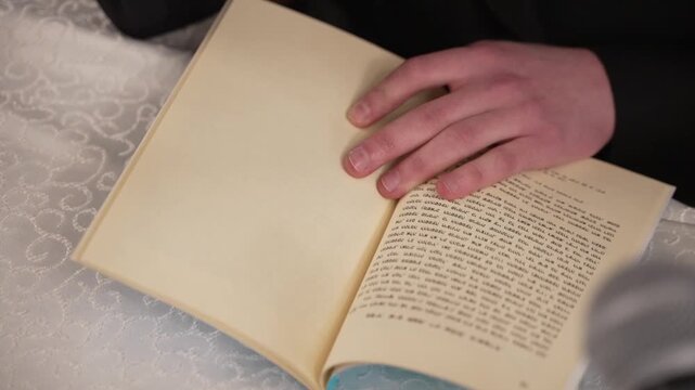 A man's hand rests on an open book with Hebrew text, with a microphone nearby. This solemn scene evokes spirituality and tradition, perfect for religious or cultural content.