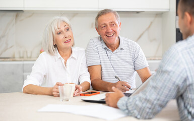 Couple of elderly man and woman while discussing deal with male salesman in kitchen