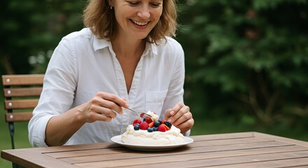 Woman enjoying pavlova dessert with fresh berries outdoors on a wooden table in summer season day time