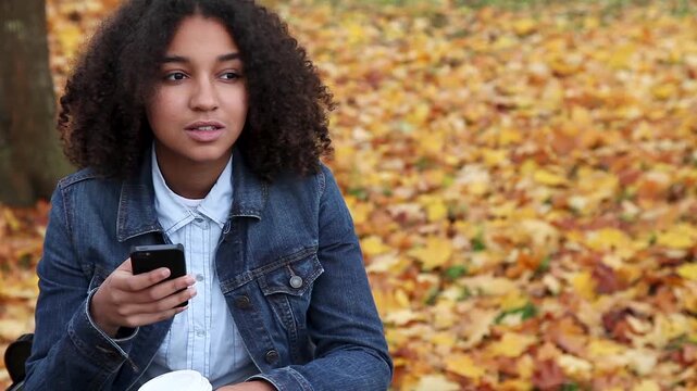 Beautiful mixed race African American girl teenager young teen wearing a blue denim jacket outside using her cell phone or smartphone for social media