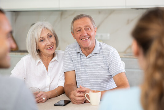 Fototapeta Smiling elderly parents and adult children sit at the table with tea and talk about home life