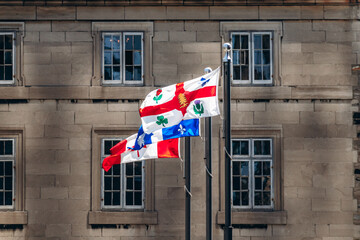 Montreal, Canada - August 11, 2025: Flag of Montreal with city symbols waving in the wind in front of a historic stone building in Old Montreal