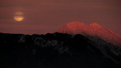 Moon rising over the mountain ridge at sunset in autumn. Kamnik Alps, Slovenia. An atmospheric landscape, perfect for illustrating tranquillity, nature themes, travel promotions, or wall art.