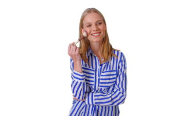 Woman standing, applying blush to her cheek with a brush. She is smiling and looking at the camera, promoting beauty and self-care