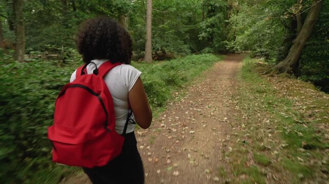 Teenage African American mixed race  girl young woman hiking with red backpack and taking photographs with a smart phone in forest woodland 