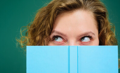 Female teacher with paper notebook. School supplies. Back to school. Education. Portrait of teacher with notepad. Student girl looking aside hiding behind hardcover book. Copy space for advertising.