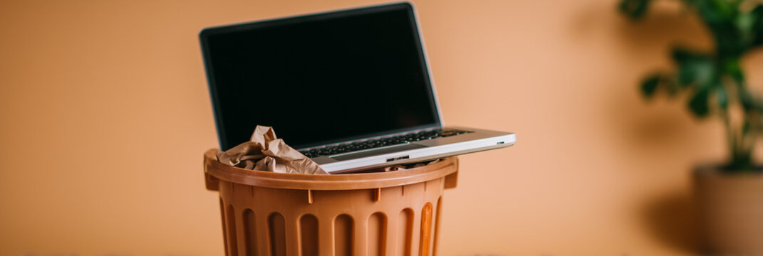 Old obsolete laptop computer discarded in a trash bin. E-waste and recycling of outdated electronic devices. Digital detox and technology frustration