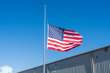 United States flag flying at half-mast on a tall flagpole against a clear blue sky. Symbol of mourning, respect, and remembrance in the United States, representing national unity and solemn tribute
