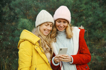 Happy two young women friends smiling with phone together, joyful girlfriends in winter day