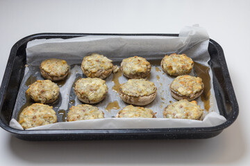 A top-down view of a dark baking tray lined with white parchment paper, neatly holding twelve stuffed mushrooms freshly taken from the oven