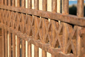 Naklejka premium Rusty iron gate detail with geometric pattern illuminated by warm light showing aged texture vintage atmosphere ideal for architectural texture themes and historic metal craftsmanship