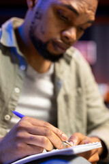 Male freelancer reviewing the financial state with data driven records and files, working from home and taking notes on his textbook. Black specialist works on a development strategy.