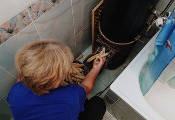 An elderly woman throws corn cobs into the stove in her bathroom.