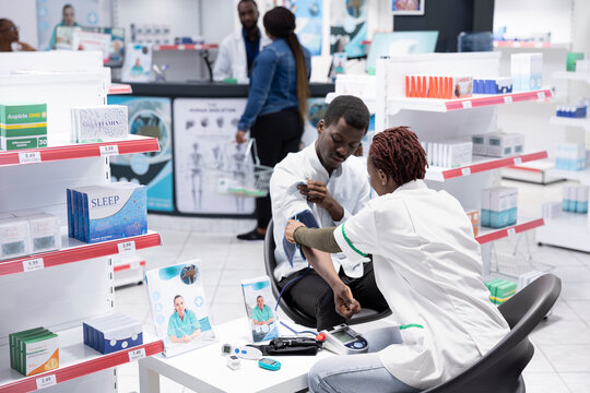 Black pharmacist providing consultation for pulse and blood pressure monitoring, using advanced professional tools in the pharmacy. Offers guidance for wellbeing and patient safety.