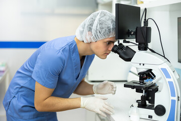 Concentrated young veterinarian using digital microscope to examine blood or skin samples of animal patient and make diagnosis in laboratory of veterinary clinic