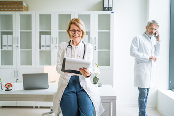 Friendly female doctor writing notes while male colleague checks phone