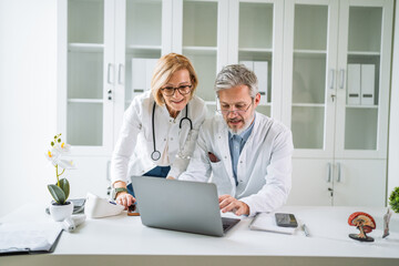 Doctors collaborating on laptop reviewing medical data in clinic