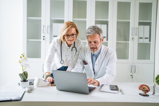 Doctors collaborating on laptop reviewing medical data in clinic