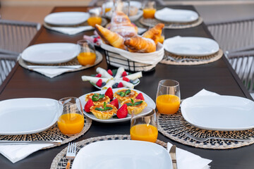 A beautifully arranged outdoor breakfast table features fresh croissants, fruit tarts, and orange juice. It's a delightful setting for a cozy morning gathering