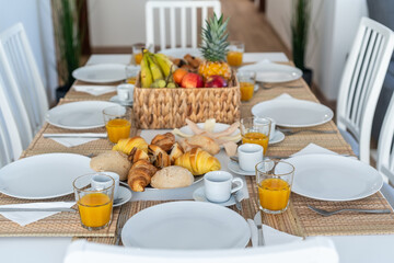 A beautifully arranged breakfast table features fresh fruits, various pastries, and beverages in a bright, modern dining space