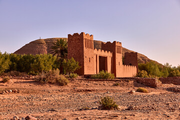 Ait ben haddou kasbah stands in the desert landscape with its traditional clay architecture. The dry riverbed is visible in front, under a clear sky in Morocco