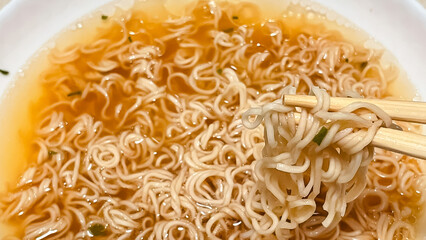 Close-up of instant ramen noodles being lifted from a bowl of golden broth with wooden chopsticks