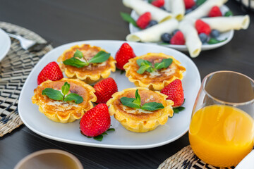 Tarts filled with creamy custard are beautifully arranged with fresh strawberries. A colorful fruit dish and drinks complete the inviting breakfast spread
