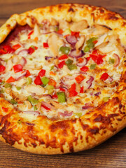 A cooked pizza with a lot of toppings including chicken, peppers, and onions. The pizza is sitting on a wooden table. Fine Italian style meal popular world wide. Rich dough base.