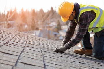 Construction worker replacing damaged roof shingles during exterior home repair, showing manual labor, safety gear, and residential building maintenance in daylight.