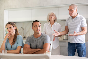 Obraz premium Elderly parents make claims to young couple in home kitchen