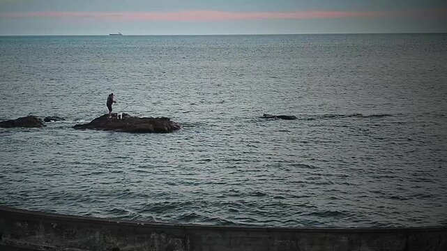 Wide shot video outdoots scene of man fishing at border of breakwater, rio de la plata river, montevideo city, uruguay