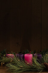 One advent candle lit with evergreen boughs and mini lights on black