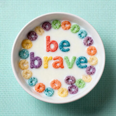 A bowl of cereal with the words be brave spelled out in colorful letter shaped cereal pieces in milk